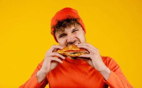 Young Handsome Hungry Man Bites Sandwich In Both Hands
