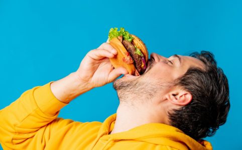 Happy White Guy In Yellow Hoodie Eating Hamburger with lab-grown Meat