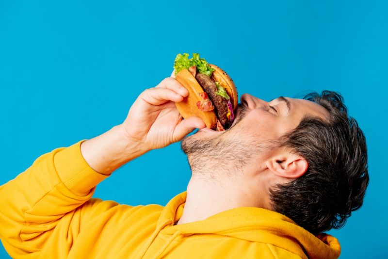 Happy White Guy In Yellow Hoodie Eating Hamburger with lab-grown Meat